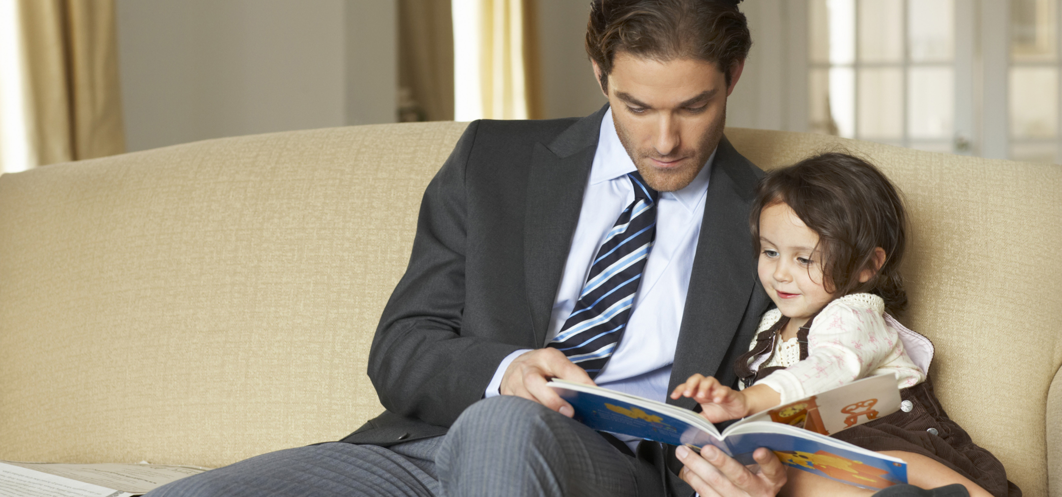 Businessman sitting on sofa reading to daughter (2-4)